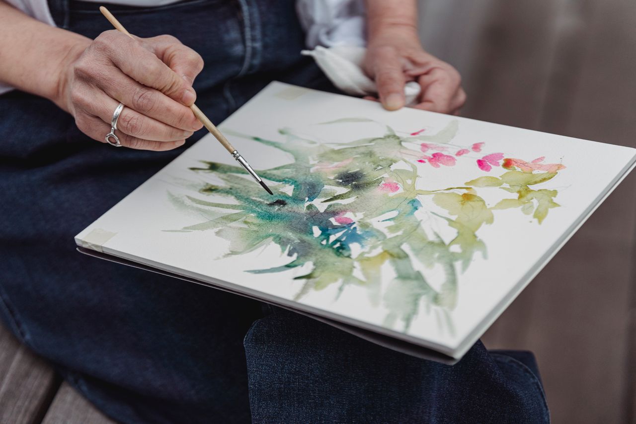 gallery-01 Close-up of an artist painting a botanical watercolor in a sketchbook, showcasing creative expression.